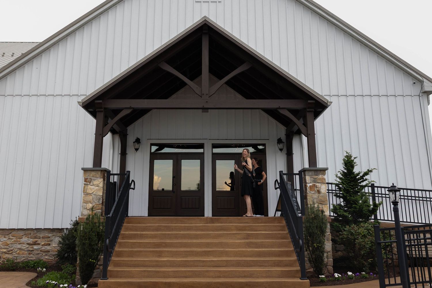 White barn-style building with covered entrance porch, stone accents, and wooden stairs leading to double doors.