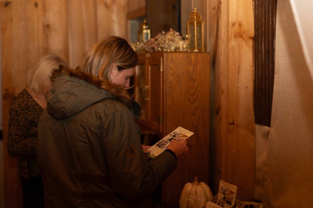 Someone in a brown hooded jacket reads a small card in a dimly lit wooden room.