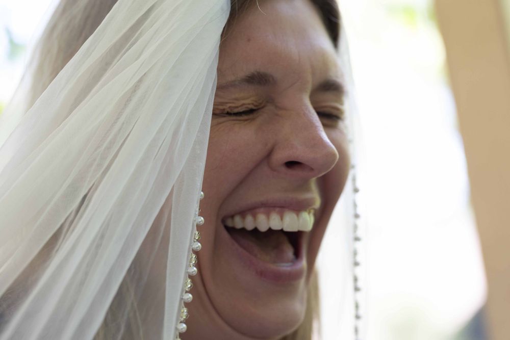 A joyful bride in white veil laughs during an intimate wedding moment.