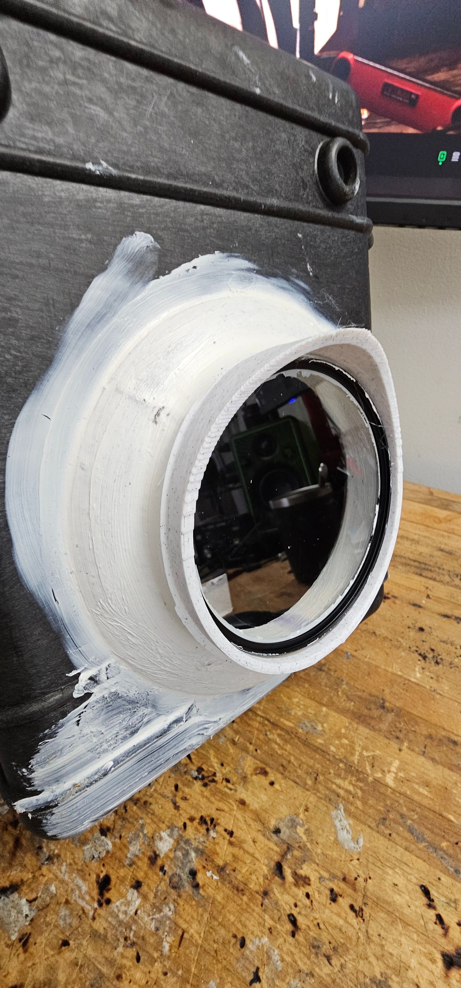 White-painted PVC pipe lens mount attached to a DIY wildlife camera trap housing on a workbench.