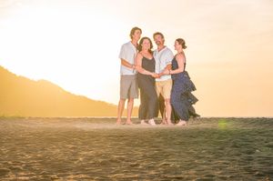 Four people smiling together on a sandy beach at golden sunset with mountains in the background.