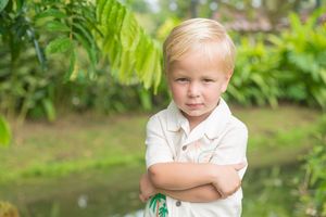 Young children in white clothing stand among vibrant green tropical foliage.