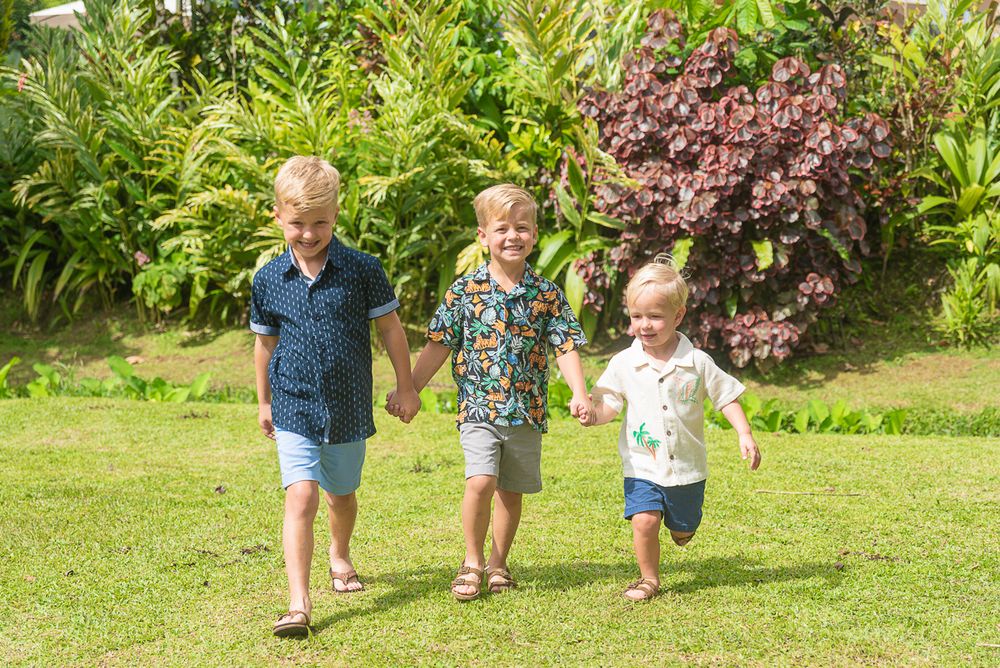Children running and playing on a grassy lawn with tropical plants and flowers in the background.