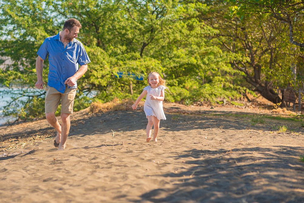 Two people running and playing together on a sandy beach with lush green trees in the background.