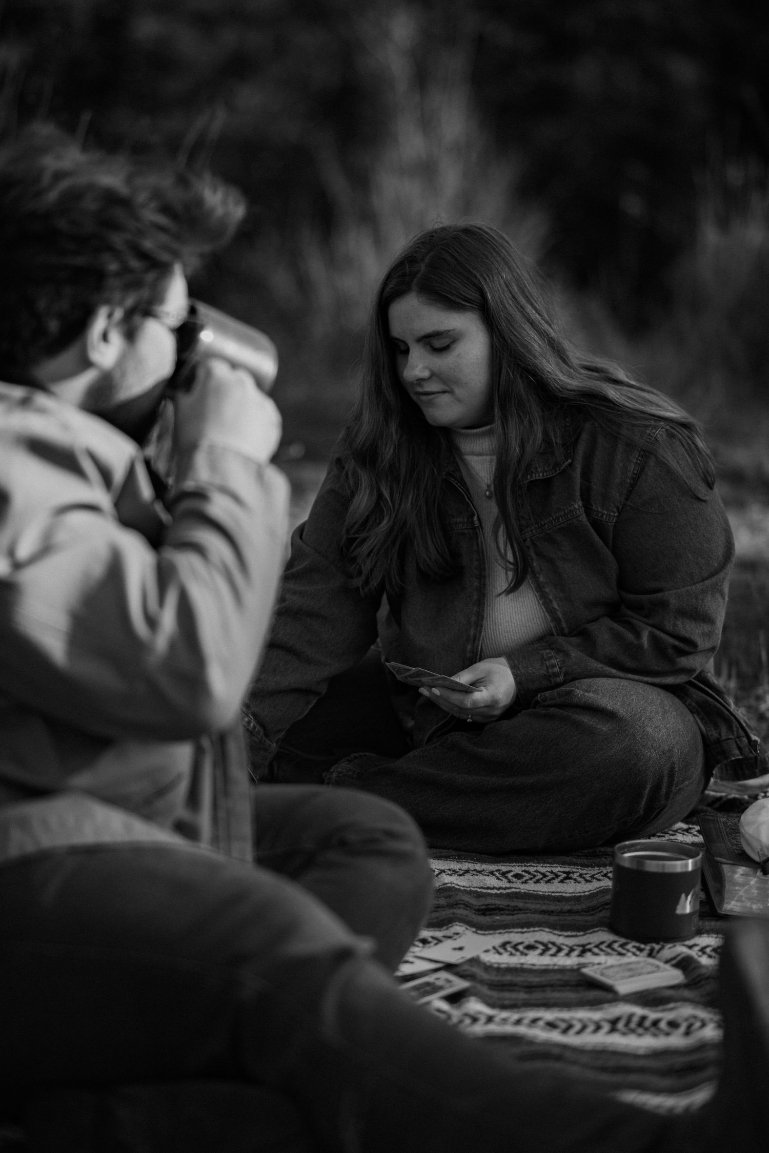 Two people sitting on a blanket in a natural setting, engaged in conversation.