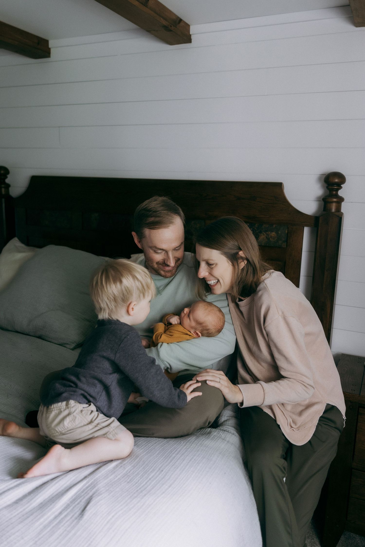 A family of four, including a mother, father, and two children, cuddling together on a bed in a cozy room.