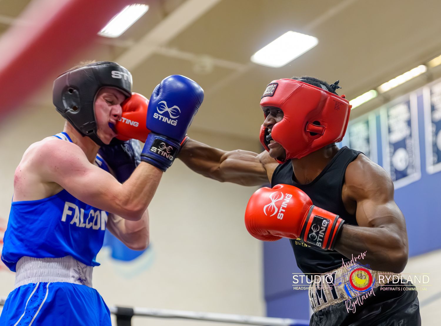 Two boxers spar in a well-lit indoor gym wearing protective headgear and gloves.