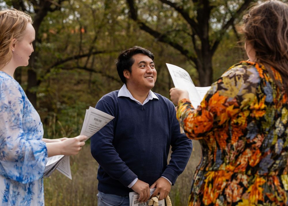 Three people holding papers in conversation outdoors among autumn trees at Platte River State Park in Louisville, NE