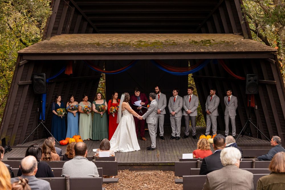 Wide shot of outdoor fall wedding ceremony on wooden stage with wedding party and seated guests  at Platte River State Park in Louisville NE