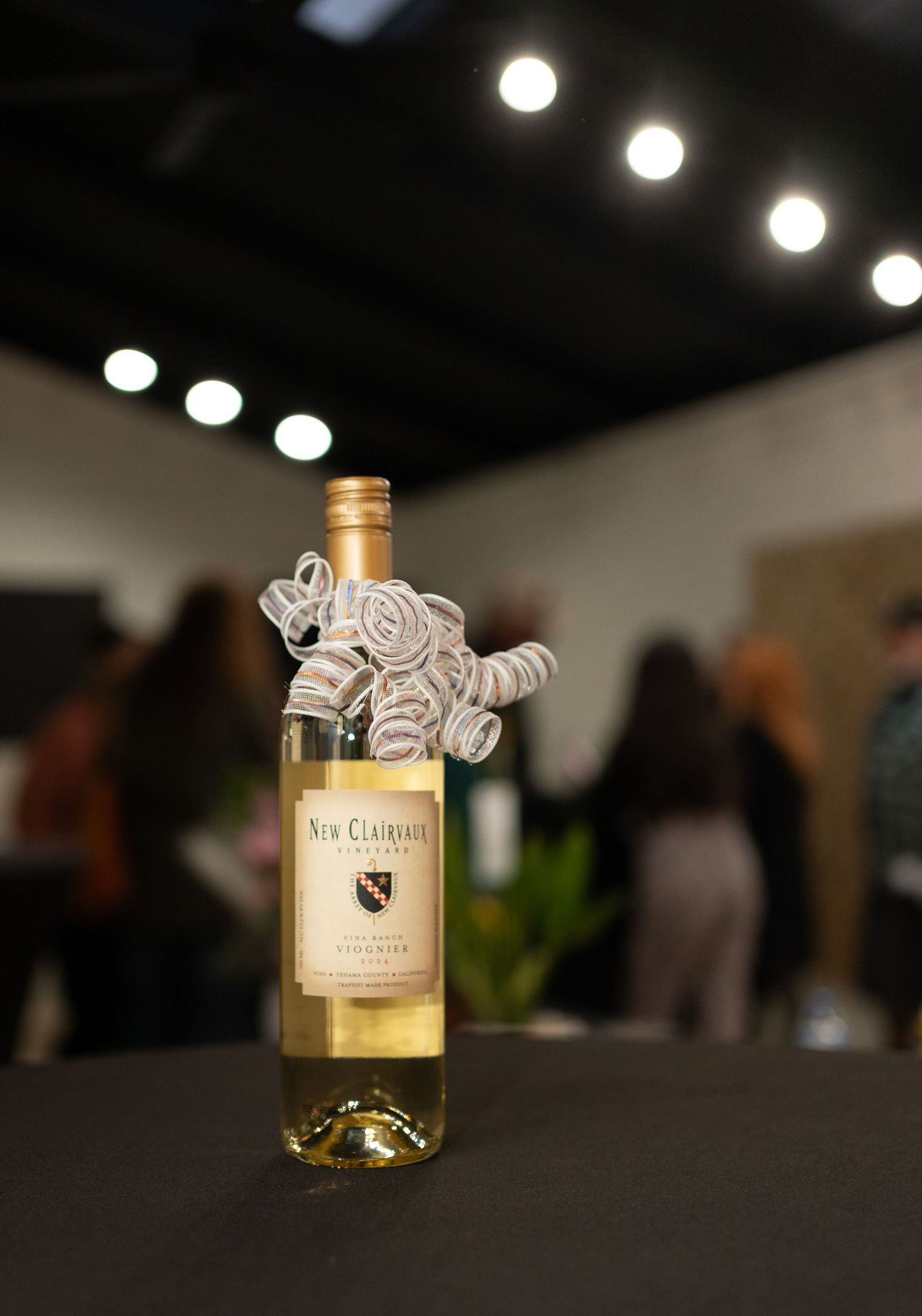 New Clairvaux Vineyard white wine bottle with ribbon bow displayed at an indoor gathering.