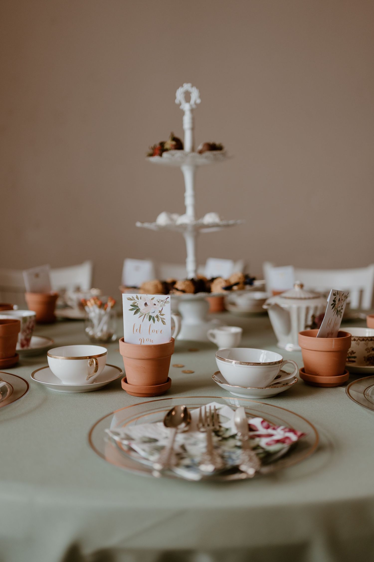Vintage tea party table setting with teacups, tiered dessert stand, and terracotta pot decor.