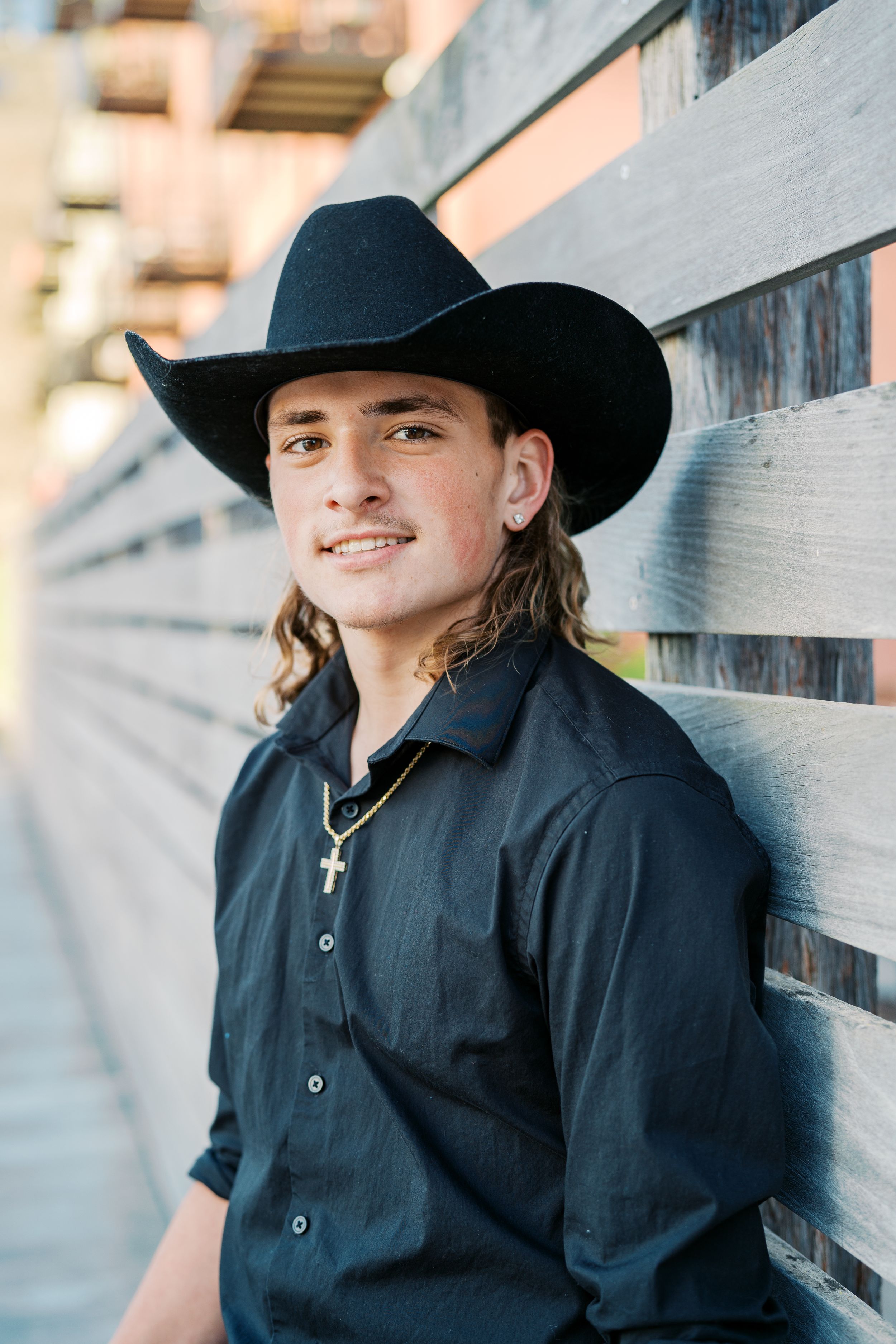 Portrait of cowboy in black shirt and hat against wooden wall.