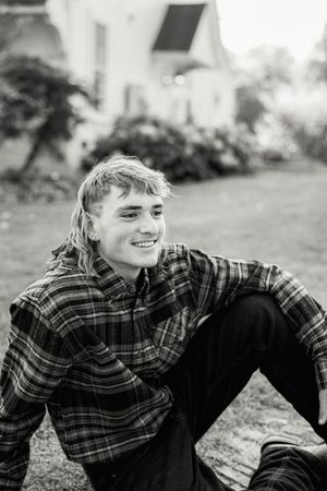 Black and white portrait of person in plaid flannel shirt sitting outdoors.