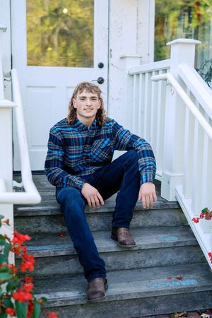 Person in blue plaid shirt sits casually on white porch steps.