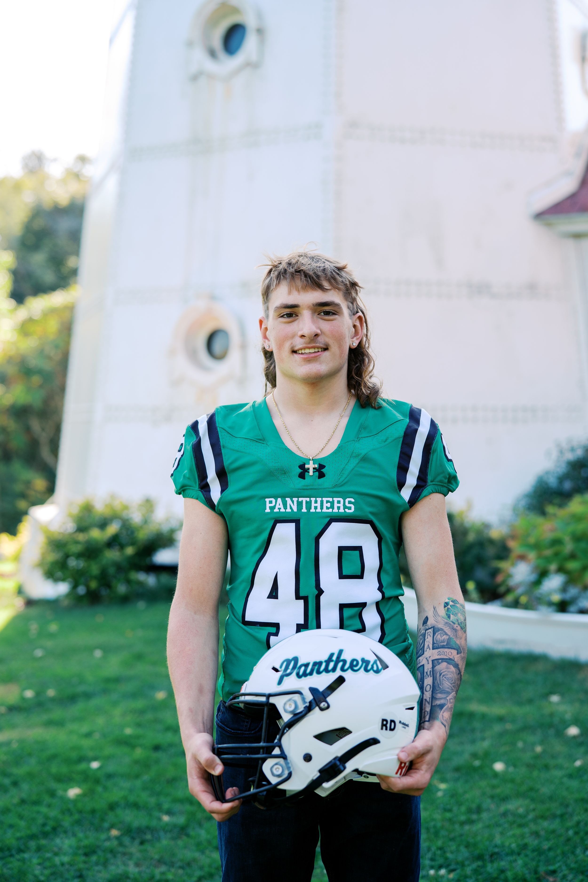 Football player wearing green Panthers jersey number 48 holding white helmet outdoors.