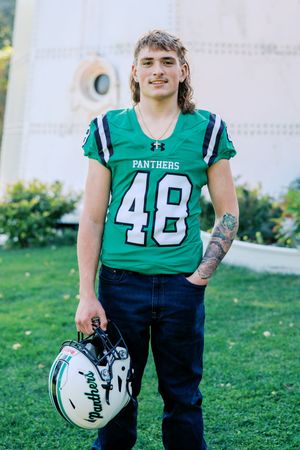 Panthers football player number 48 posing with helmet on grassy field.