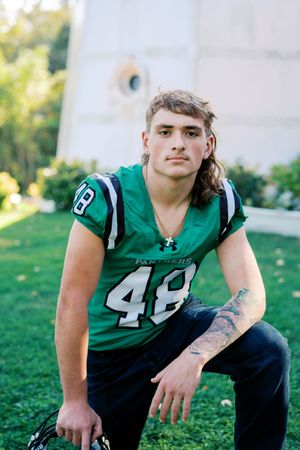 Football player in green Panthers uniform posing on grass near white building.