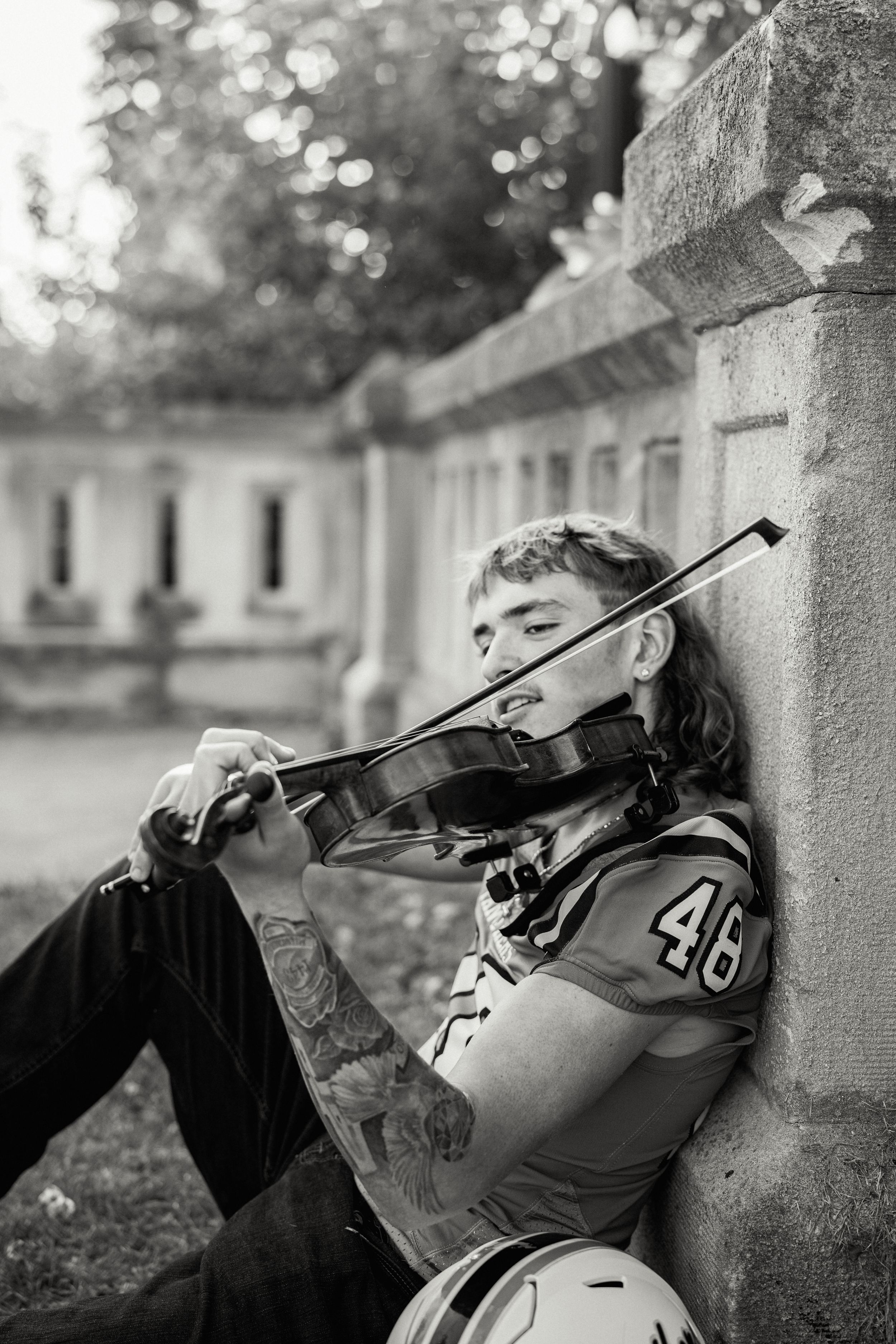 Black and white photo of musician playing violin while resting against stone column.