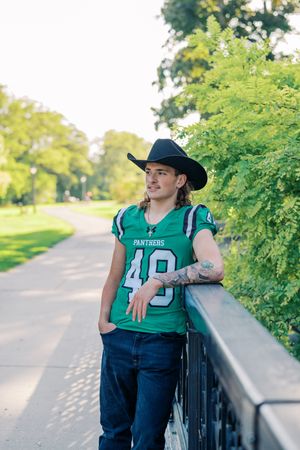 Athlete in Panthers jersey and cowboy hat posing along tree-lined path.