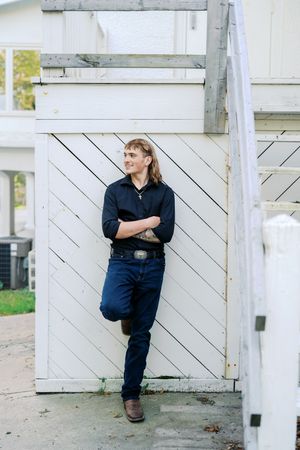 Person in dark clothing poses against white diagonal wooden wall.