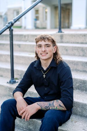Person in dark clothing sits on concrete steps with tattoos visible.