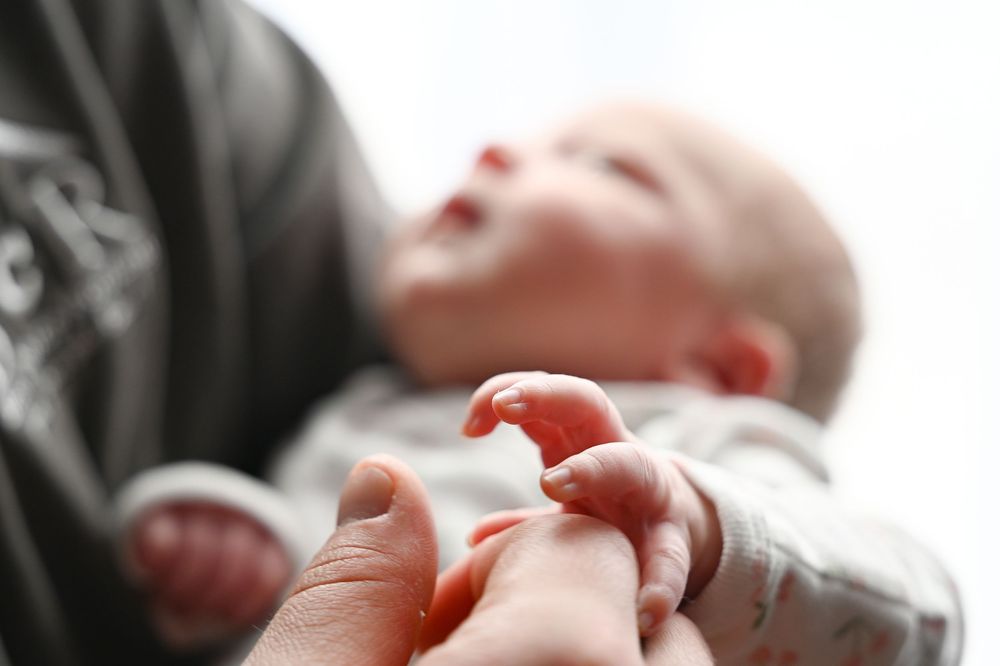 A tiny infant's hand grasps an adult's finger while resting peacefully in black and white tones.