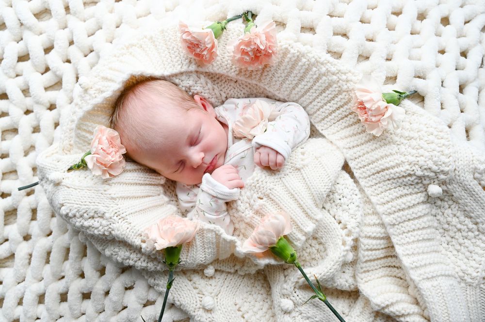 Baby resting on white knitted blanket with pink and green floral accents.
