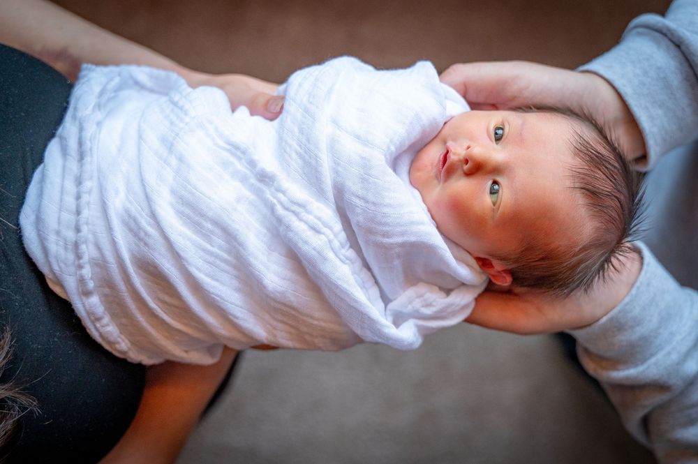 A series of seven candid photos showing a baby in white clothing lying on a dark background.