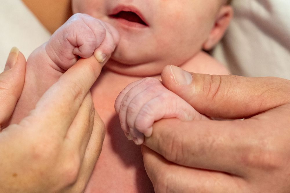 Close-up of adult hands gently holding and examining tiny newborn baby fingers.