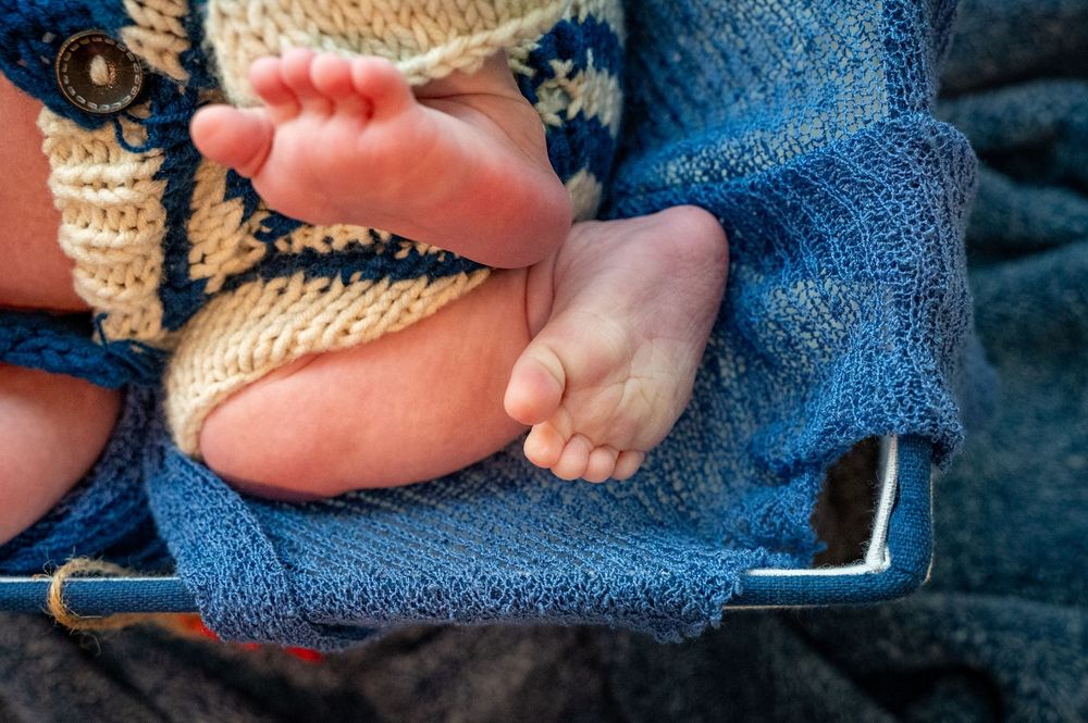 Tiny baby feet rest on blue fabric next to a knitted beige garment.