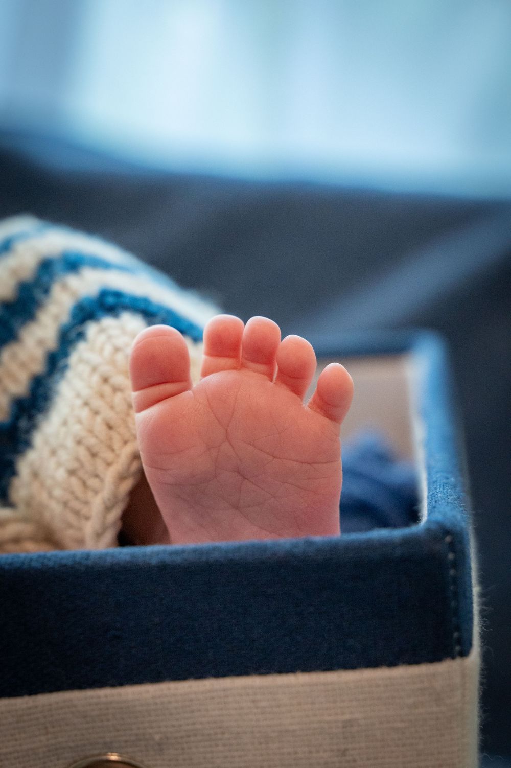Close-up view of a tiny baby foot wearing a knitted sock against a blurred blue background.