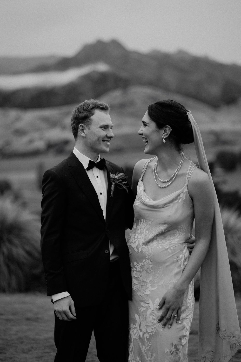 A couple in formal wedding attire share intimate moments against a scenic mountain backdrop at Lookout Lodge in Wanaka, Otago wedding venue.