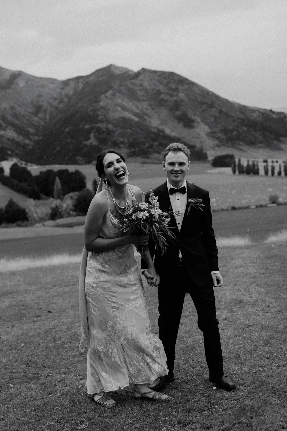 Black and white wedding photo of a couple at Lookout Lodge in Wanaka, Otago wedding venue, laughing together against mountain scenery.
