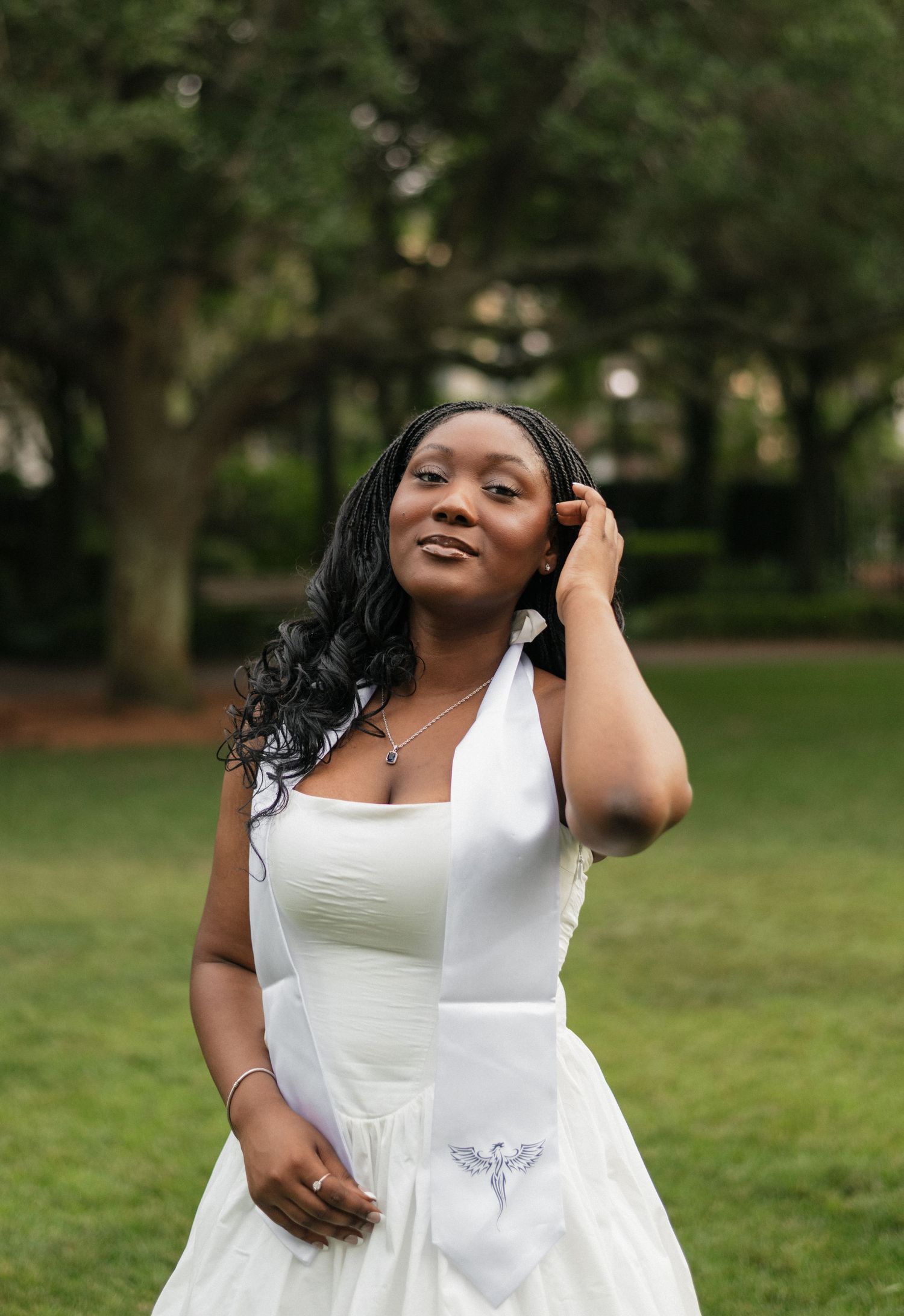 A woman in a flowing white dress twirls joyfully in a sunlit park setting.
