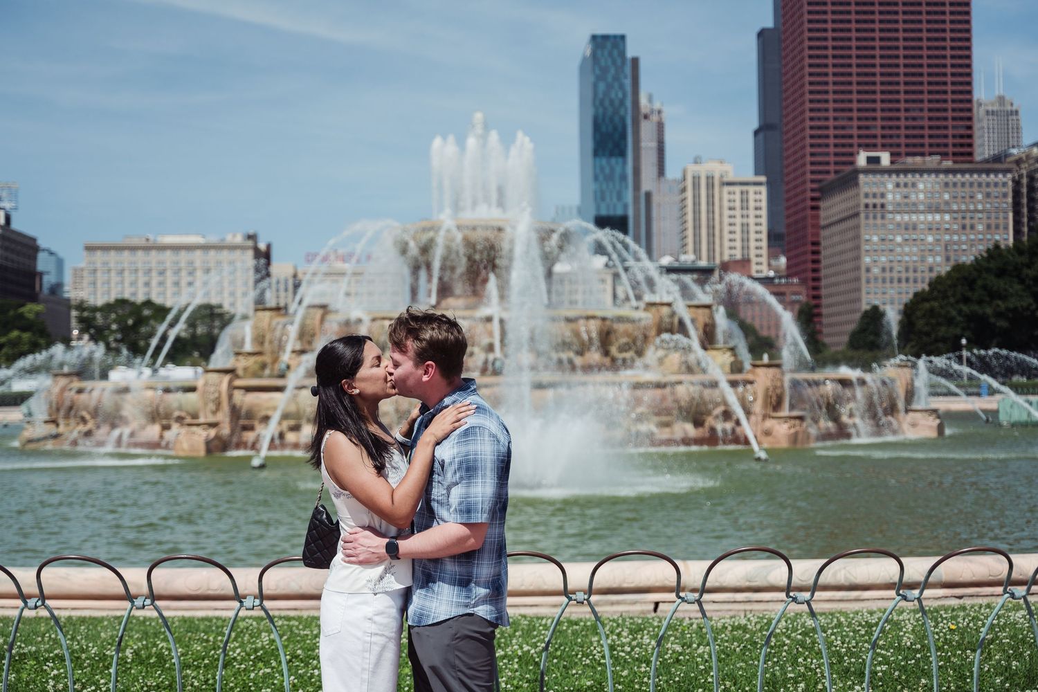 Couple embraces in front of Buckingham Fountain at Grant Park in downtown Chicago on a sunny summer day.