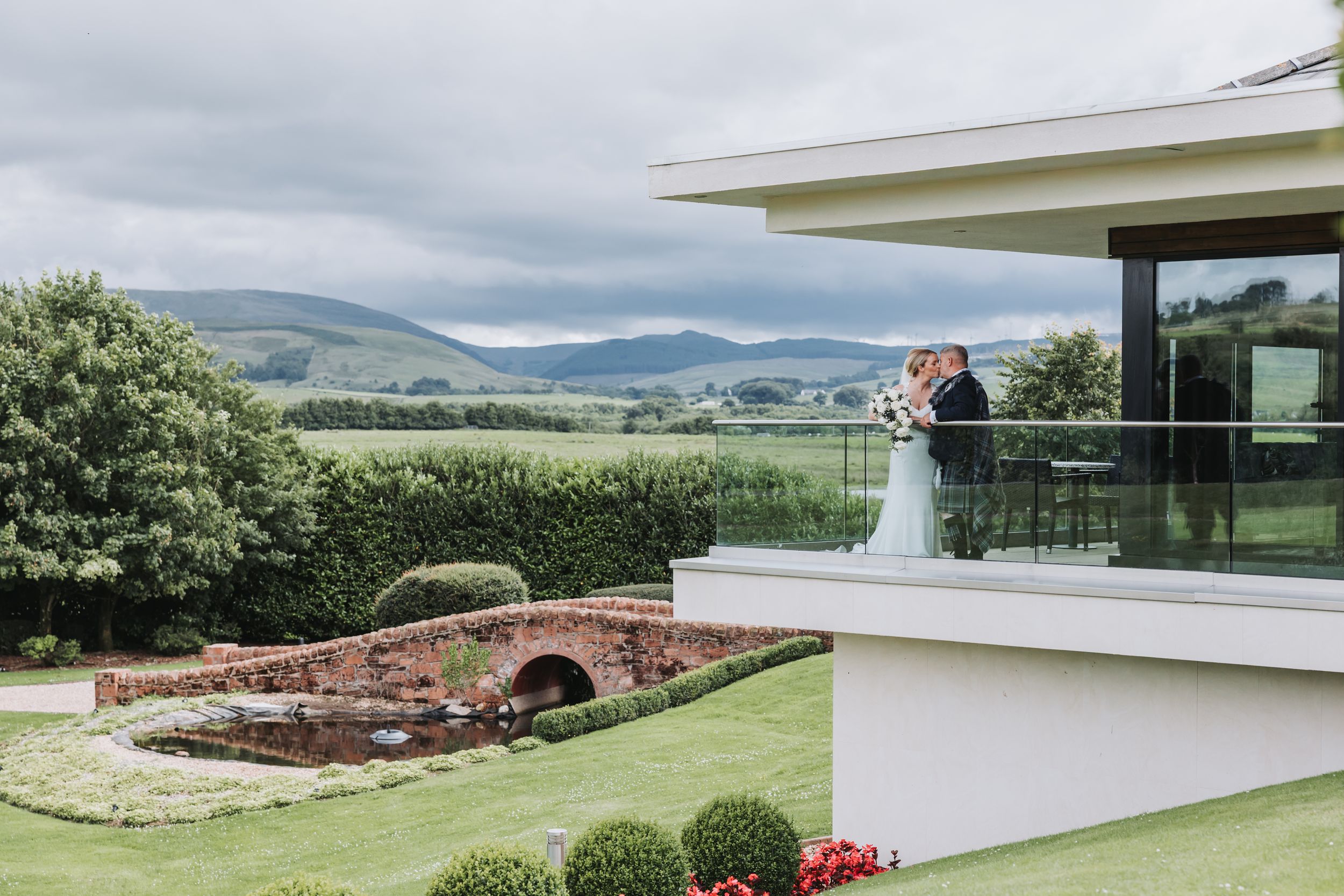 Scenic outdoor wedding venue with rolling hills and mountains in the background features elegant white decor and seating.