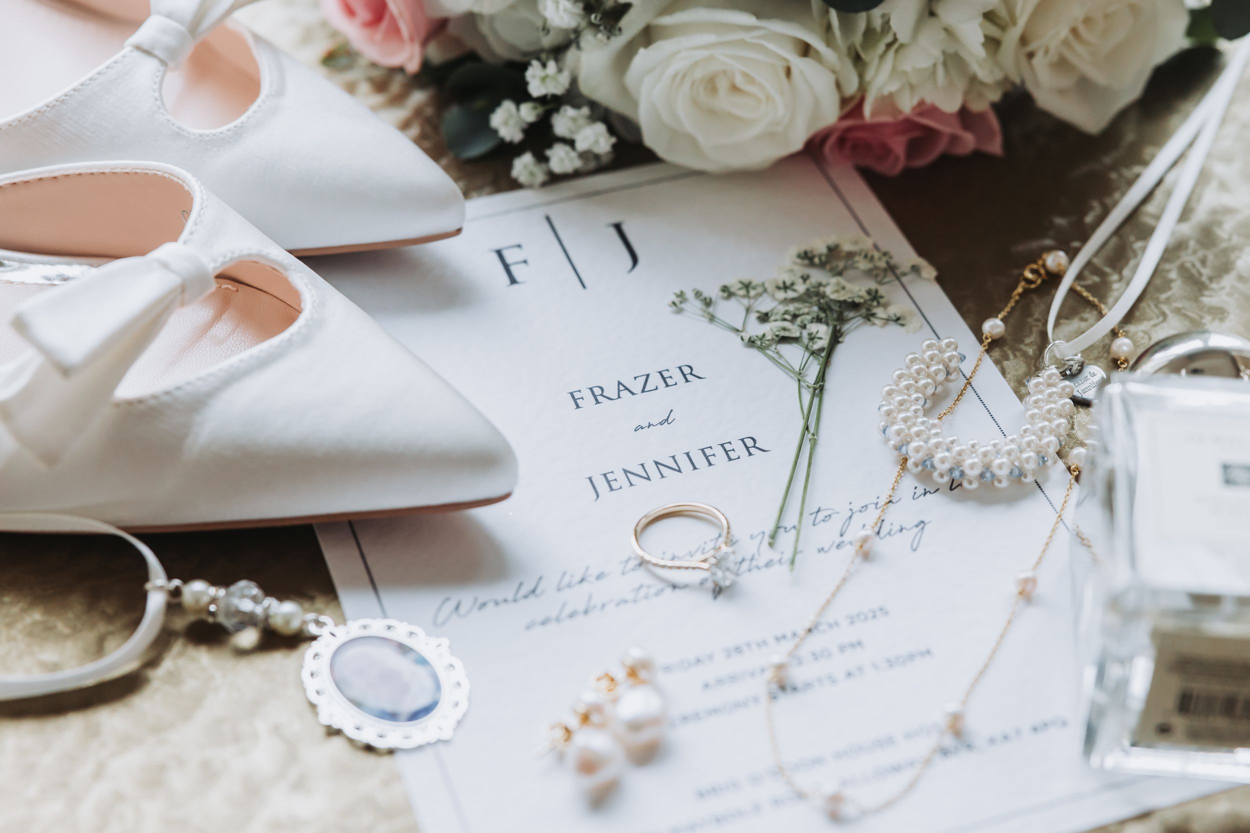 Elegant wedding details featuring white roses, delicate stationery, and soft pink accents arranged on a light surface.