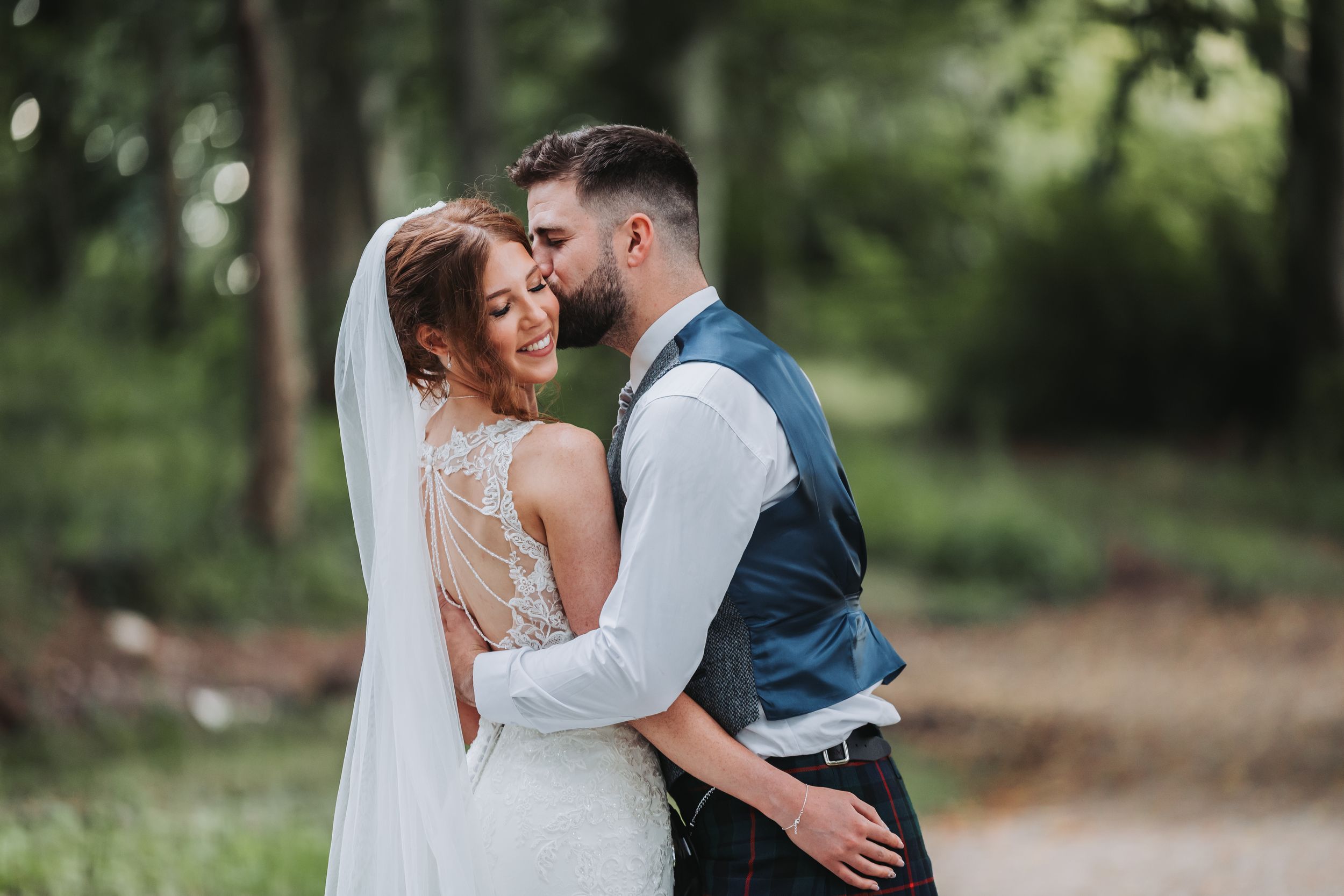 A romantic wedding couple embraces outdoors in a natural setting surrounded by lush greenery.