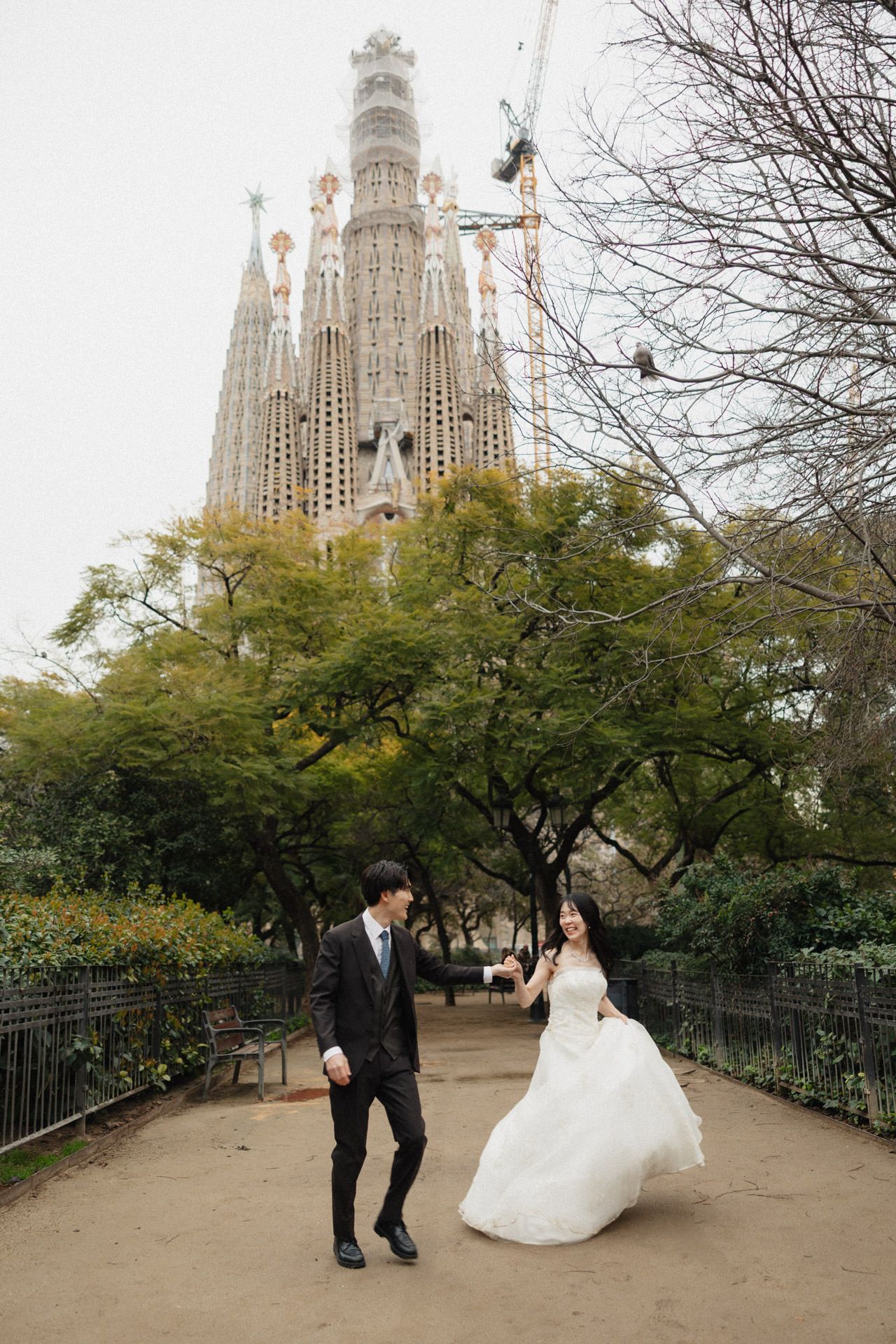 A couple in wedding attire poses for romantic photos in front of the iconic Sagrada Familia cathedral in Barcelona.