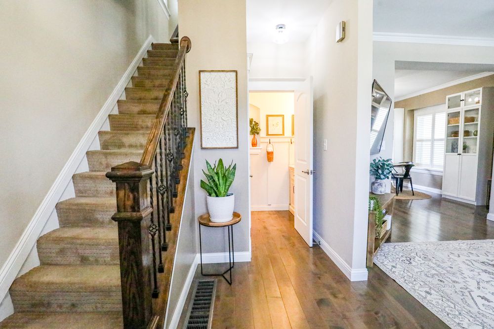 Modern home interior featuring carpeted stairs with dark wood railing, hardwood floors and bright hallway leading to living area.