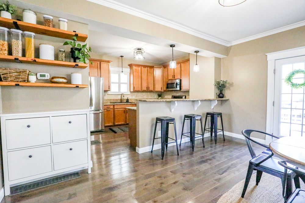Modern kitchen and dining area with wood flooring, white walls, and open concept layout featuring floating shelves.