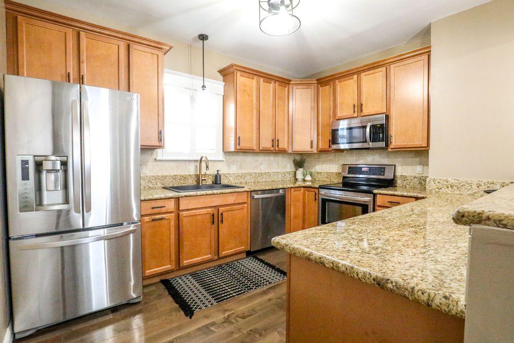 Panoramic view of a modern kitchen with granite countertops, stainless steel appliances, and honey-colored wood cabinets.