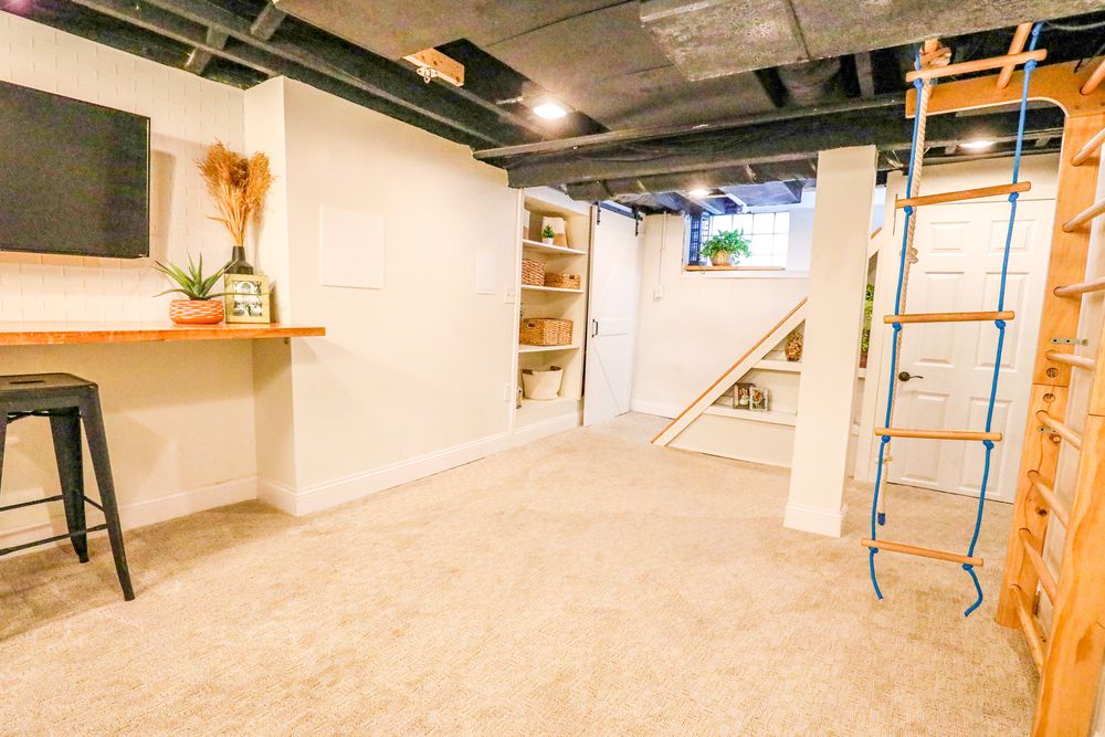 Unfinished basement renovation shows exposed ceiling joists, concrete floor, and wooden support posts in progress.