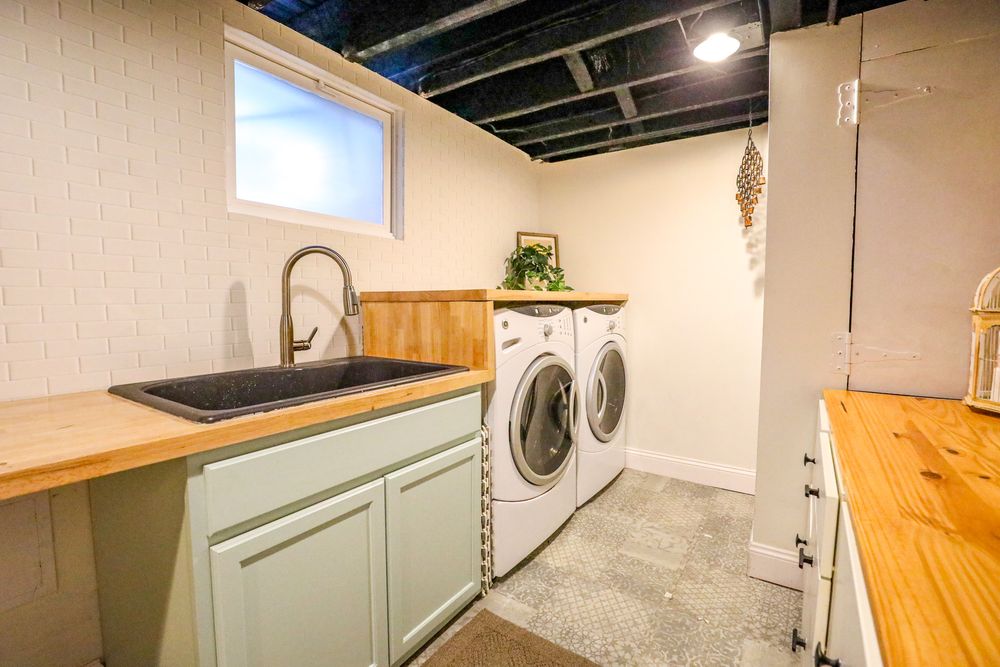 Modern laundry room with stacked washer and dryer units, wooden countertops, and light mint green cabinets.