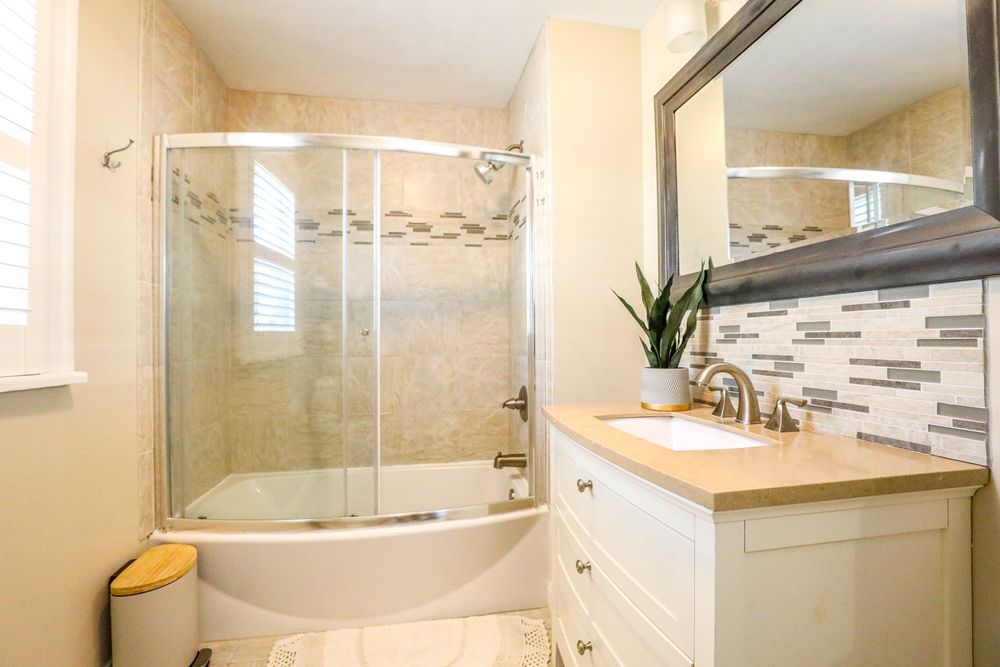 Modern bathroom renovation featuring glass shower enclosure, tiled walls, and contemporary fixtures in neutral tones.