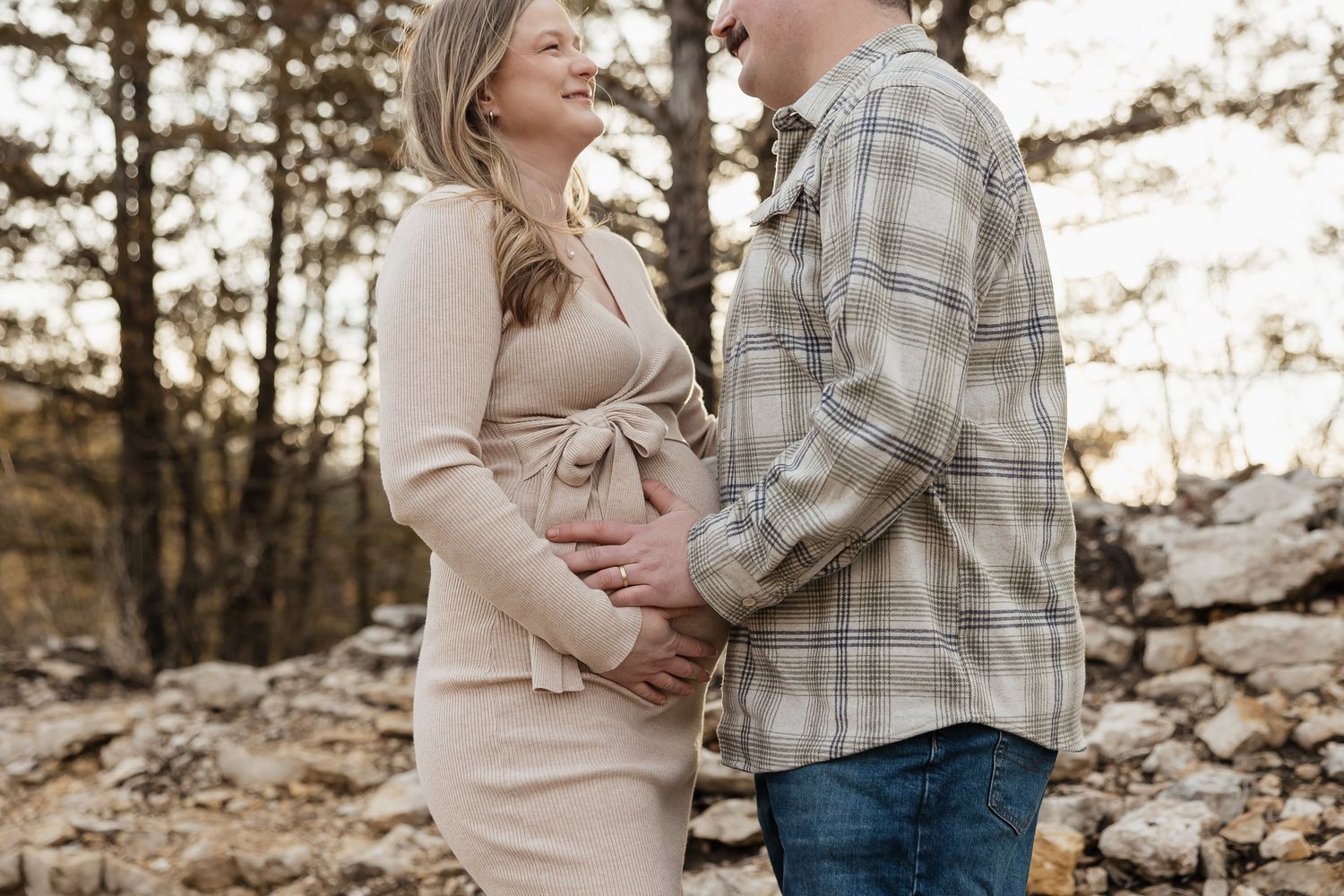 pregnant mother to be holds baby bump with dad in front of pine trees during photo session