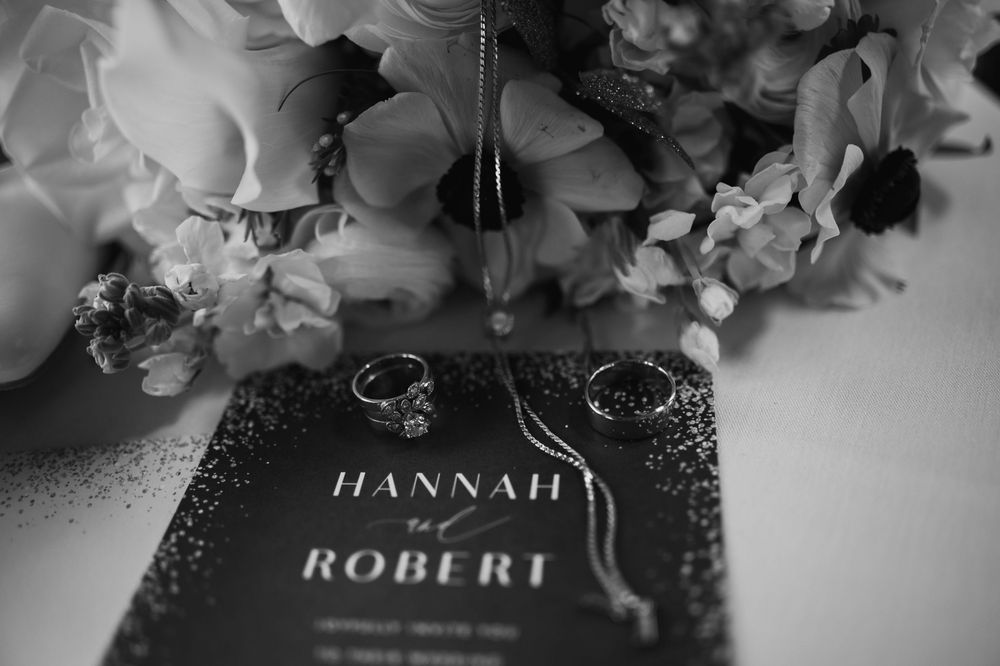 Black and white photo of wedding rings and bouquet on Hannah and Robert wedding invitation card.