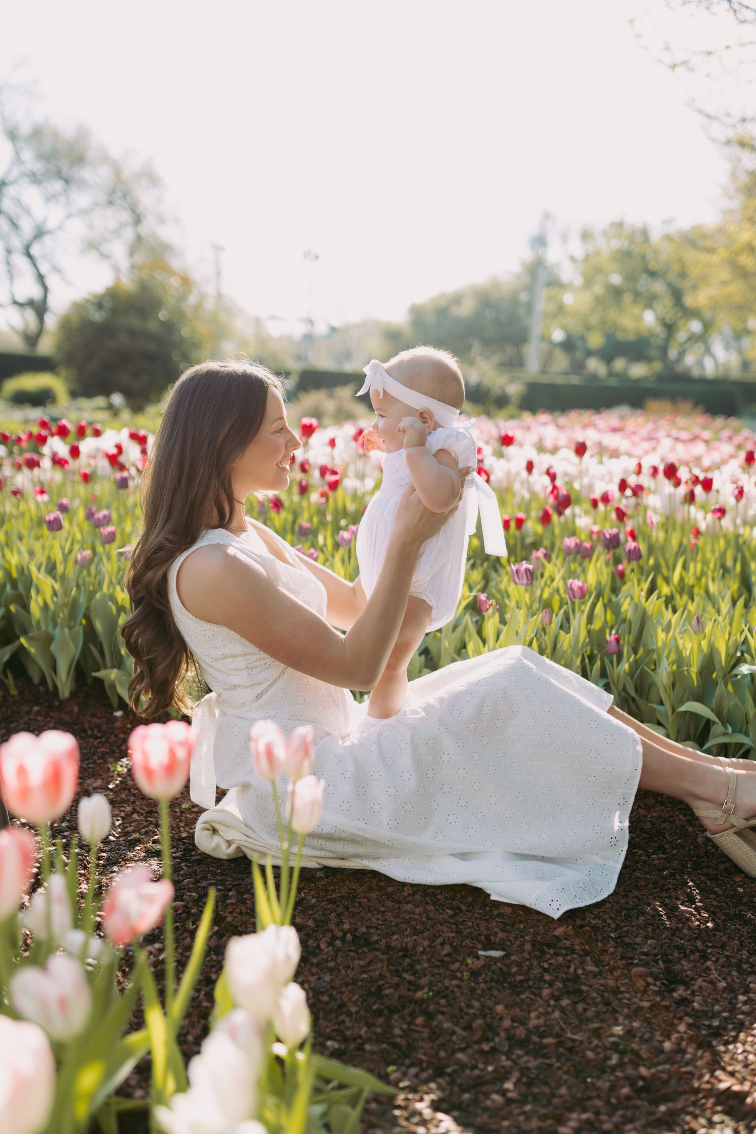 A tender moment between parent and baby surrounded by blooming pink and red tulips in a spring garden.