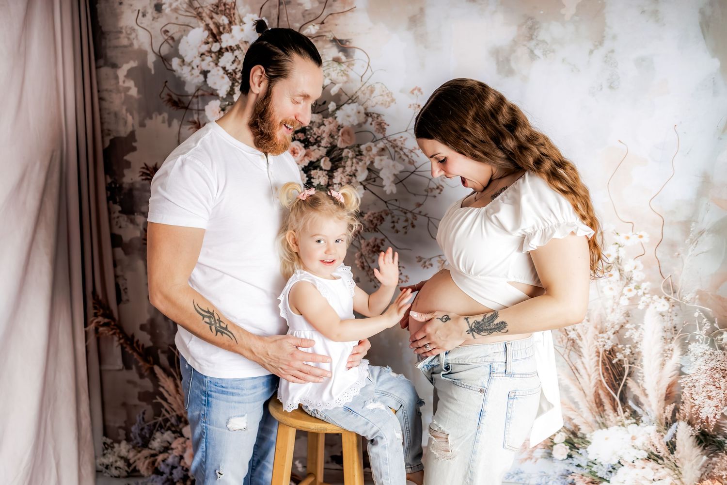 A family in white and denim poses together against a dreamy floral backdrop with dried pampas grass and neutral tones.