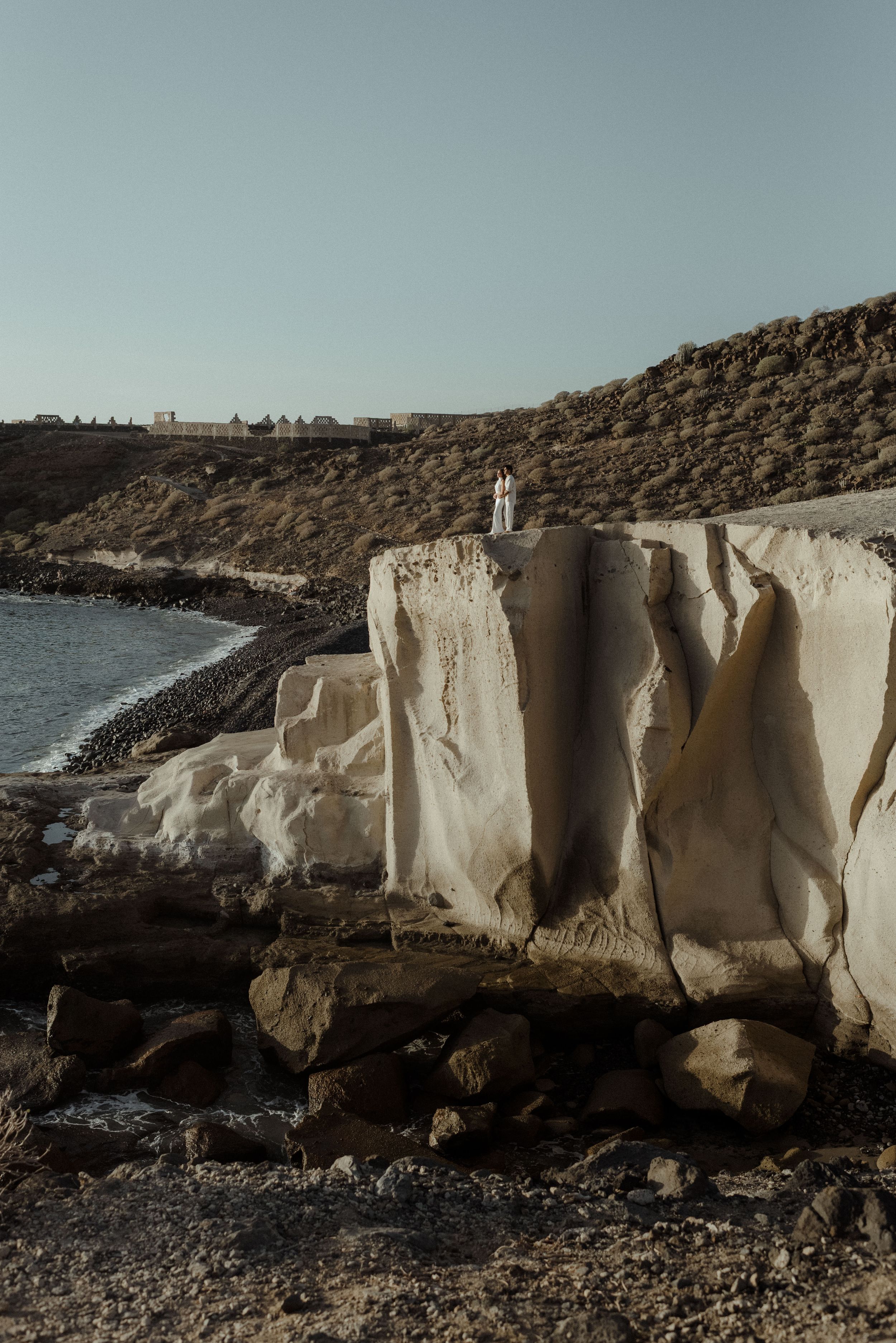 Dramatic white limestone cliffs rise above a rocky shoreline, creating a striking coastal landscape against a moody sky.